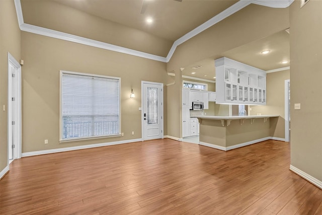 unfurnished living room featuring baseboards, ornamental molding, a ceiling fan, and light wood finished floors