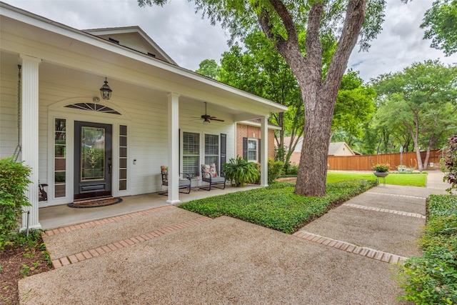 view of exterior entry featuring a porch, a ceiling fan, and fence