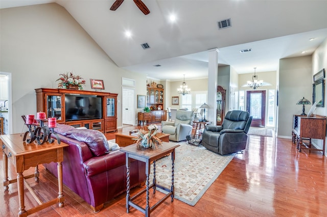 living room featuring ornate columns, ceiling fan with notable chandelier, wood finished floors, visible vents, and high vaulted ceiling