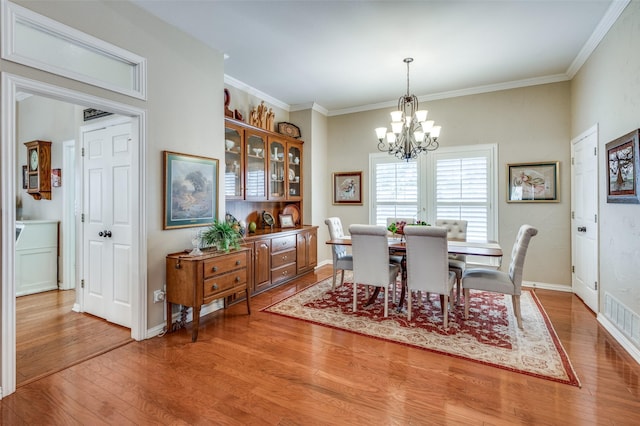 dining room featuring a chandelier, crown molding, baseboards, and wood finished floors