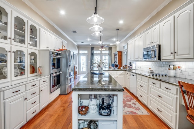 kitchen with appliances with stainless steel finishes, glass insert cabinets, a center island, decorative light fixtures, and white cabinetry