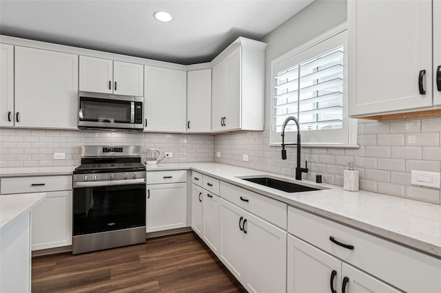 kitchen featuring dark wood-style flooring, stainless steel appliances, white cabinetry, a sink, and light stone countertops