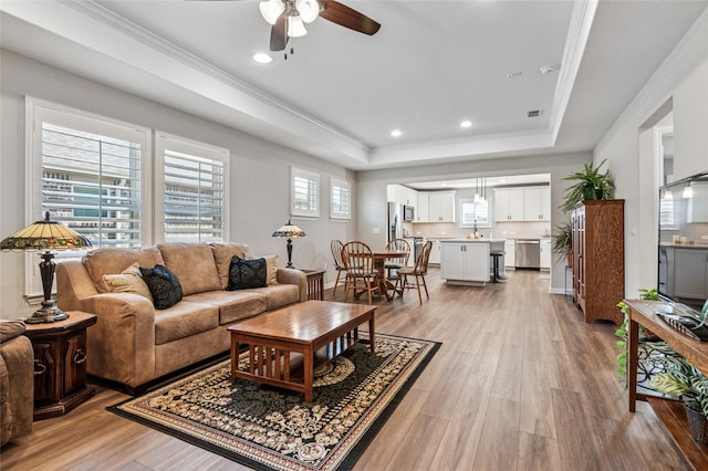 living room featuring ornamental molding, light wood finished floors, and a raised ceiling