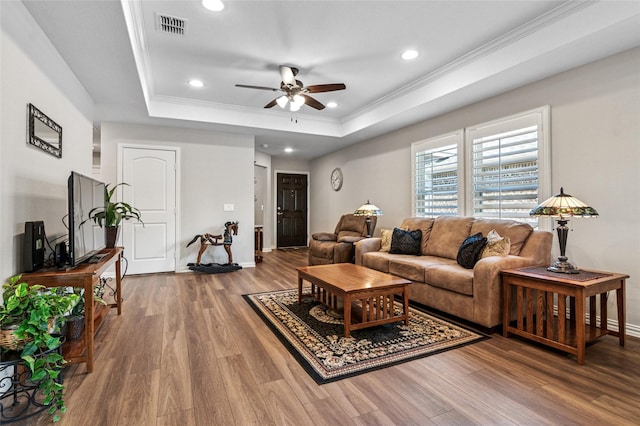 living room with wood finished floors, visible vents, a ceiling fan, ornamental molding, and a tray ceiling