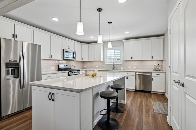 kitchen featuring a kitchen island, appliances with stainless steel finishes, dark wood-style flooring, decorative light fixtures, and white cabinetry