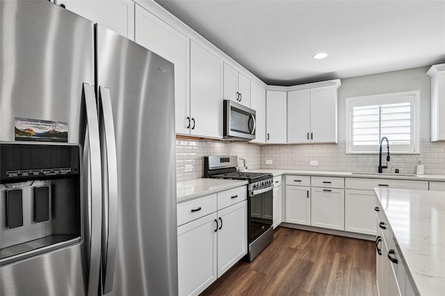 kitchen with a sink, white cabinets, appliances with stainless steel finishes, backsplash, and light stone countertops