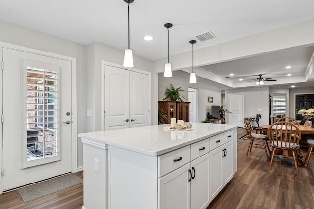 kitchen with visible vents, white cabinets, a kitchen island, a tray ceiling, and pendant lighting