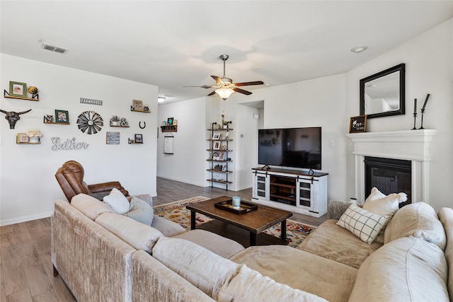 living room featuring a glass covered fireplace, ceiling fan, wood finished floors, and visible vents