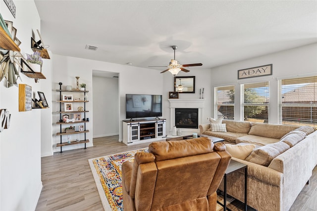 living area featuring visible vents, baseboards, a glass covered fireplace, ceiling fan, and light wood-type flooring