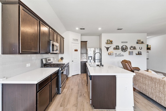 kitchen with dark brown cabinets, a sink, stainless steel appliances, open floor plan, and light wood-type flooring