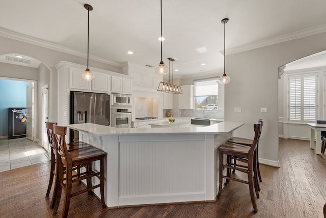 kitchen featuring arched walkways, stainless steel appliances, white cabinets, a large island, and tasteful backsplash