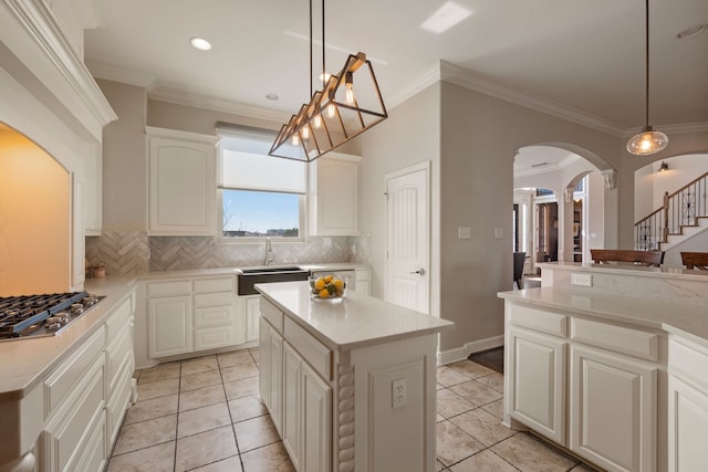 kitchen featuring arched walkways, decorative backsplash, light countertops, stainless steel gas stovetop, and a sink