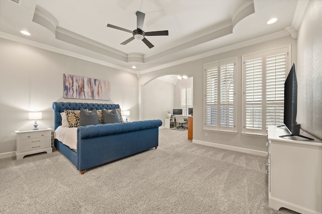 carpeted bedroom with ornamental molding, a tray ceiling, arched walkways, and baseboards