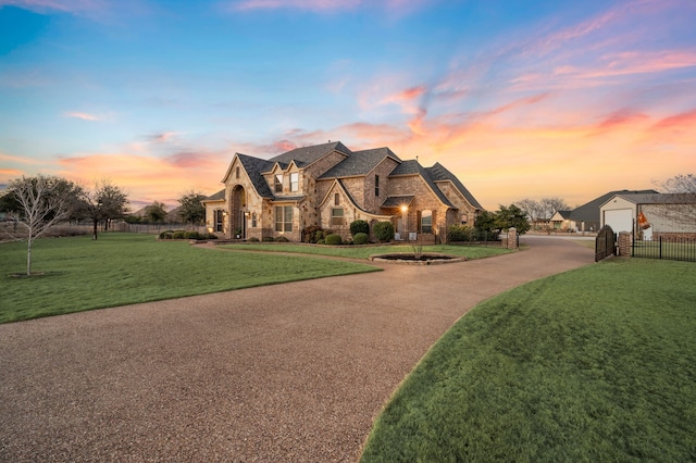 french country home with a yard, stone siding, fence, and driveway