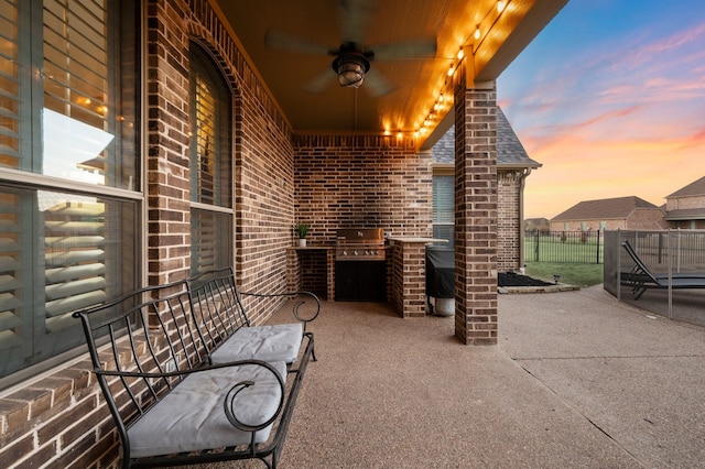 view of patio featuring a ceiling fan, a grill, fence, and an outdoor kitchen