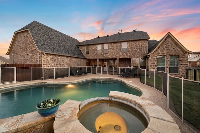 pool at dusk with a patio area, fence, and a pool with connected hot tub