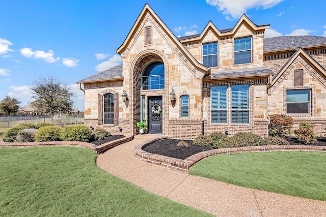 view of front facade featuring stone siding, brick siding, roof with shingles, and a front yard