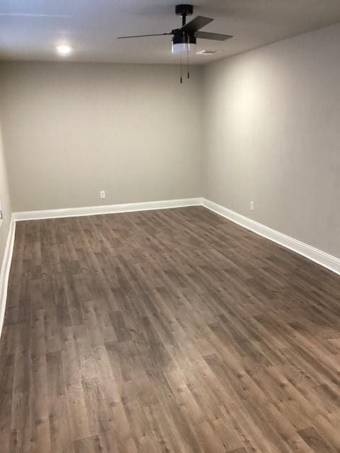 empty room with dark wood-style floors, a ceiling fan, and baseboards