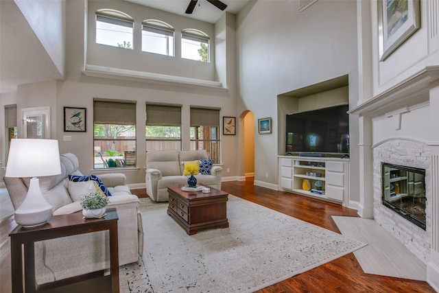 living room with a wealth of natural light, wood finished floors, a stone fireplace, and arched walkways