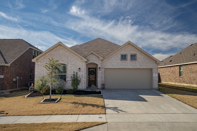 french country style house with brick siding, a shingled roof, and driveway