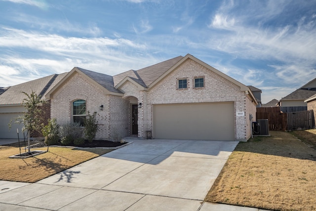 french provincial home featuring fence, a garage, central air condition unit, concrete driveway, and brick siding