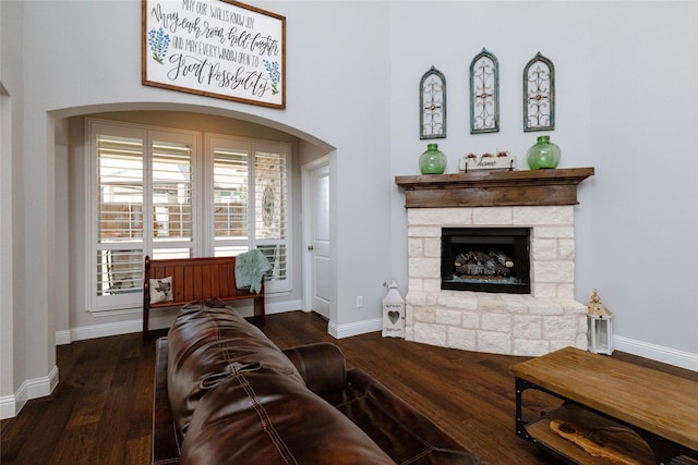 living area with dark wood-style flooring, baseboards, a fireplace, and arched walkways