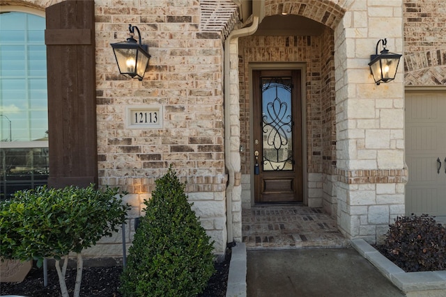 doorway to property with stone siding, an attached garage, and brick siding