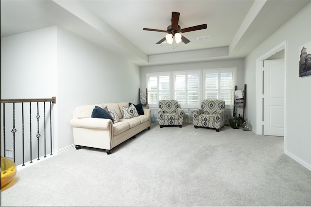 living area featuring ceiling fan, baseboards, light carpet, and a tray ceiling