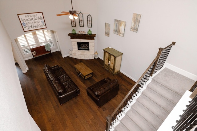 living room featuring dark wood-style flooring, baseboards, a fireplace, and ceiling fan