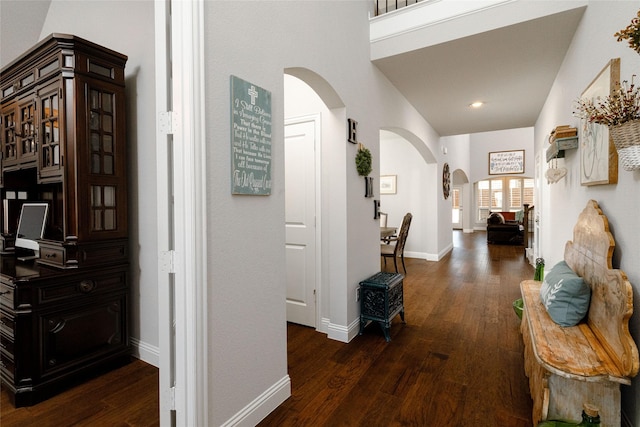 hall with dark wood finished floors, baseboards, a towering ceiling, and arched walkways