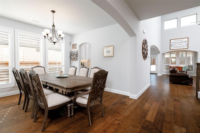 dining space with visible vents, baseboards, a chandelier, arched walkways, and dark wood-style flooring