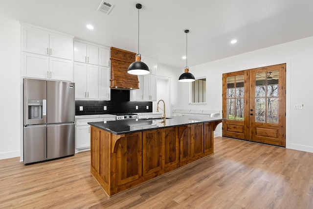 kitchen with dark countertops, visible vents, white cabinets, an island with sink, and stainless steel fridge