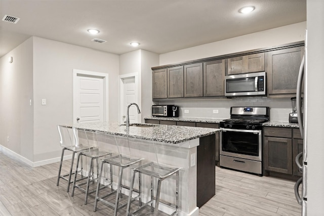 kitchen featuring a sink, light stone counters, visible vents, a center island with sink, and appliances with stainless steel finishes