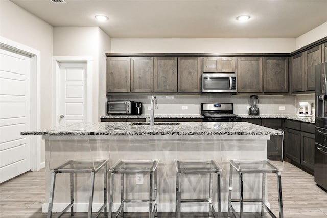 kitchen featuring light stone counters, a breakfast bar area, appliances with stainless steel finishes, and an island with sink