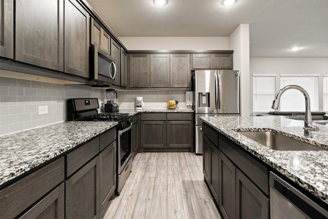 kitchen featuring tasteful backsplash, stainless steel appliances, a sink, light wood-style floors, and light stone counters