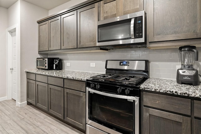 kitchen featuring dark brown cabinetry, light stone counters, appliances with stainless steel finishes, and decorative backsplash