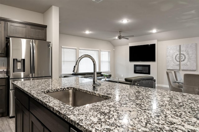 kitchen with a sink, stone countertops, dark brown cabinetry, stainless steel fridge, and a glass covered fireplace