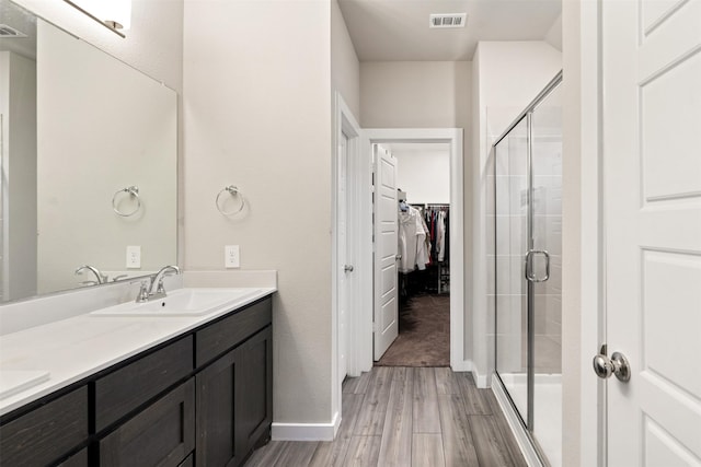 full bathroom featuring visible vents, a walk in closet, a sink, a stall shower, and wood finished floors