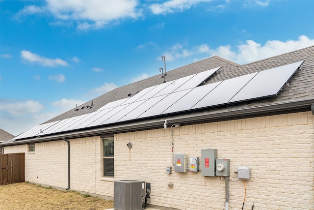 view of property exterior with roof mounted solar panels, a shingled roof, cooling unit, and brick siding