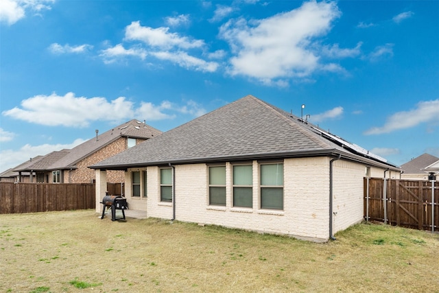 rear view of property with roof with shingles, a lawn, a fenced backyard, and brick siding