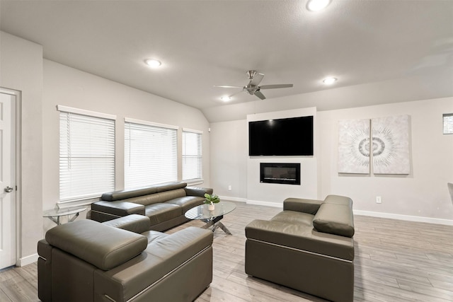 living room with a ceiling fan, baseboards, a glass covered fireplace, light wood finished floors, and vaulted ceiling