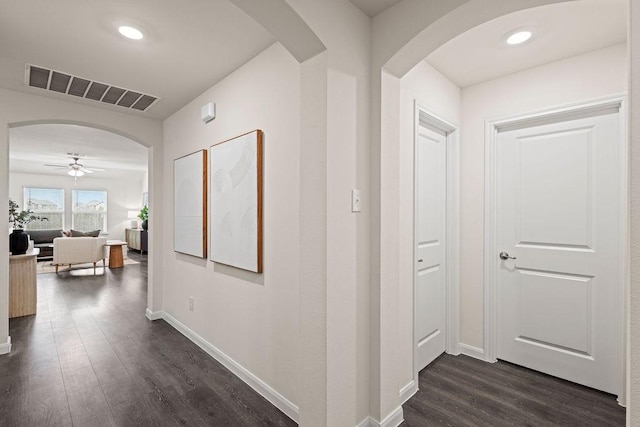 corridor with baseboards, visible vents, arched walkways, dark wood-type flooring, and recessed lighting