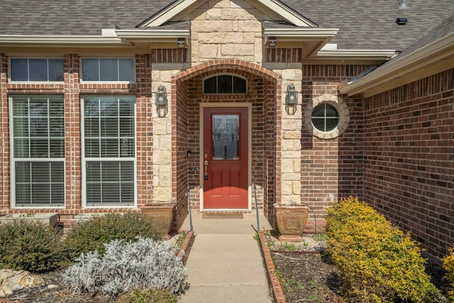 entrance to property featuring brick siding and a shingled roof