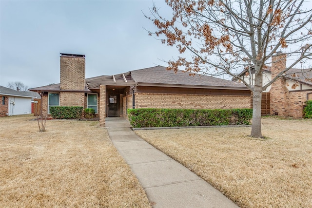 ranch-style house featuring brick siding, a chimney, a shingled roof, and a front yard