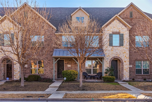 townhome / multi-family property featuring stone siding, brick siding, and roof with shingles