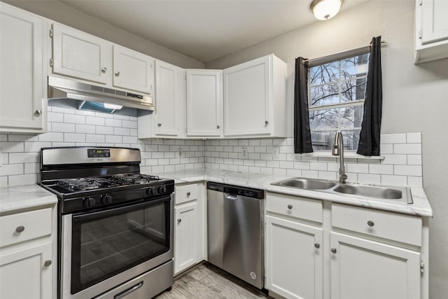 kitchen with a sink, under cabinet range hood, appliances with stainless steel finishes, white cabinetry, and decorative backsplash