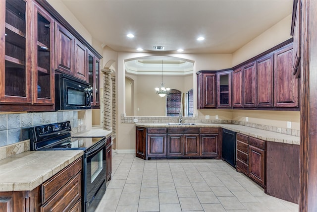 kitchen with a sink, light countertops, black appliances, glass insert cabinets, and pendant lighting