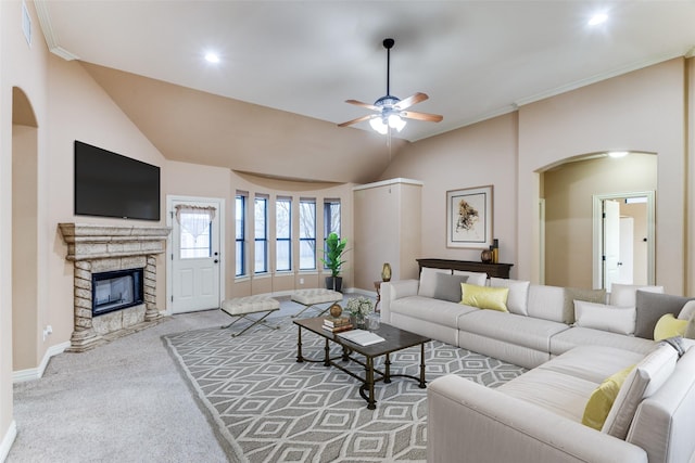 living room featuring ceiling fan, crown molding, a stone fireplace, and light colored carpet