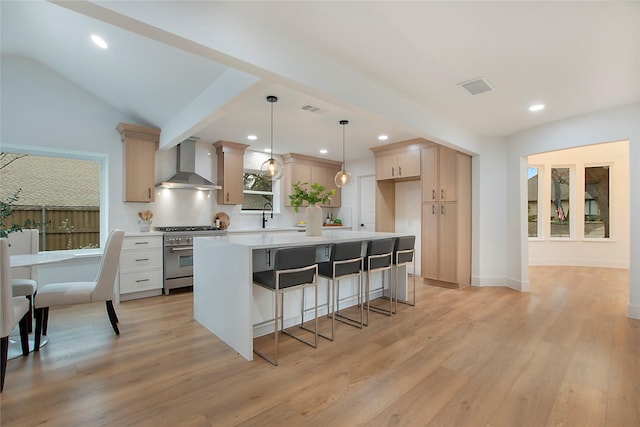 kitchen featuring a kitchen island, stainless steel range, hanging light fixtures, wall chimney range hood, and light countertops