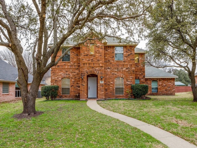 traditional home with a shingled roof, a front yard, brick siding, and fence